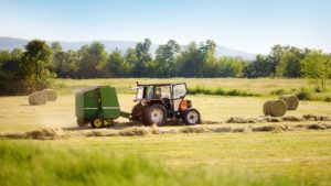 tractor con un coloso recogiendo silos de campo en una pampa verde de campo con árboles al fondo fomentando el desarrollo rural