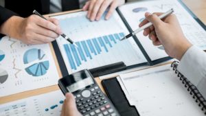 Gráficos de preparación y evaluación de proyectos sobre una mesa con dos manos de hombres sujetando lápices y una calculadora